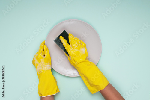 woman in yellow cleaning gloves on light color background cleaning plate with cleaning sponge