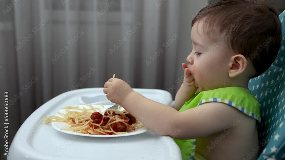 adorable kid baby boy eating pasta spaghetti with meatballs from beef or drinking water from bottle.tasty delicious food toddler with green bib take food with hands putting in mouth.hungry child adorable kid baby boy eating pasta spaghetti with meatballs from beef or drinking water from bottle.tasty delicious food toddler with green bib take food with hands putting in mouth.hungry child