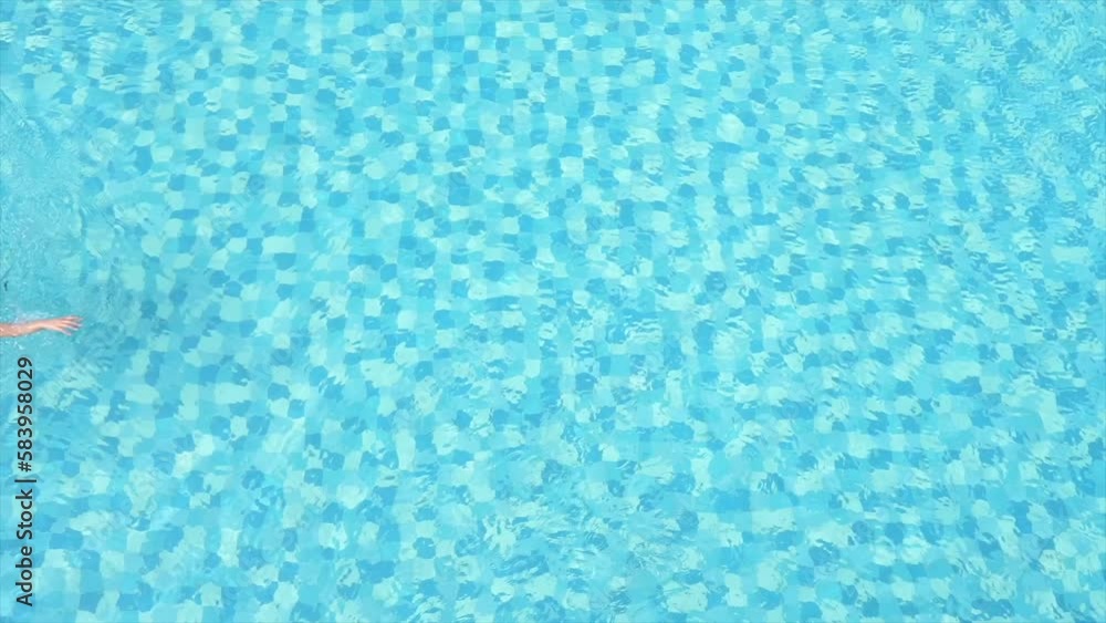 Top view of a crystal-clear blue pool with a female South Asian athlete swimming across Top view of a crystal-clear blue pool with a female South Asian athlete swimming across