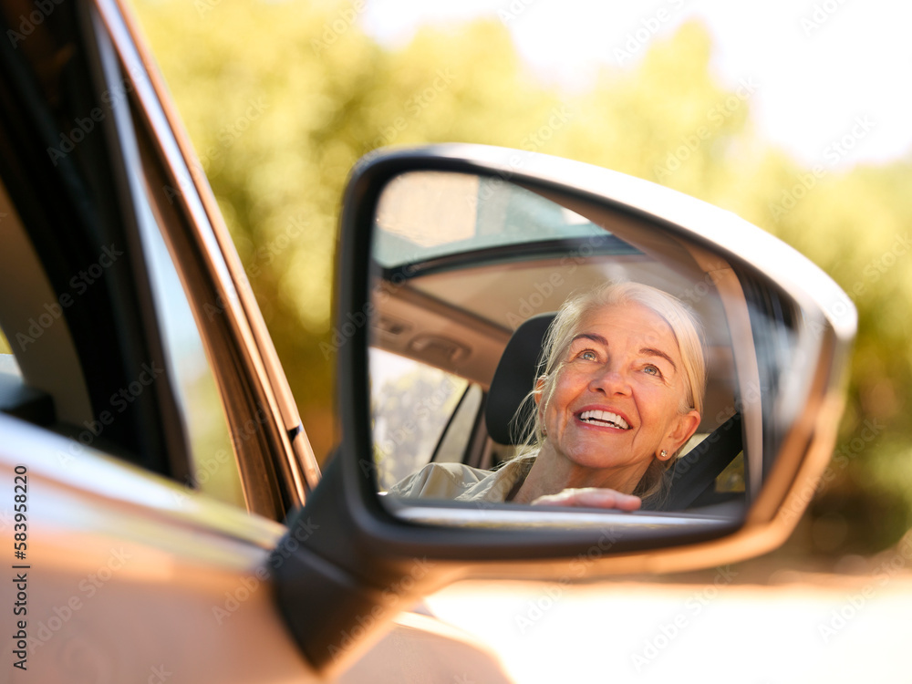 Smiling Senior Female Driver Reflected In Wing Mirror Of Car Enjoying Day Trip Out Driving