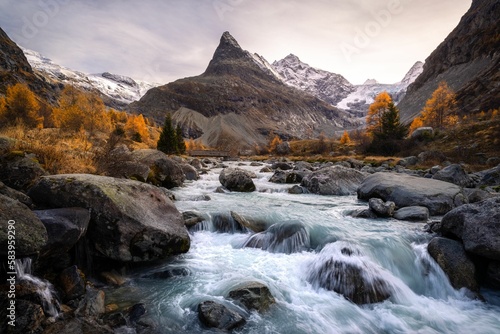 Valley of Ferpecle in autumn before sunset, with a river surrounded by golden larches
