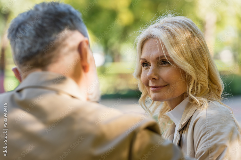 Smiling blonde woman looking at blurred husband in spring park. Smiling blonde woman looking at blurred husband in spring park.
