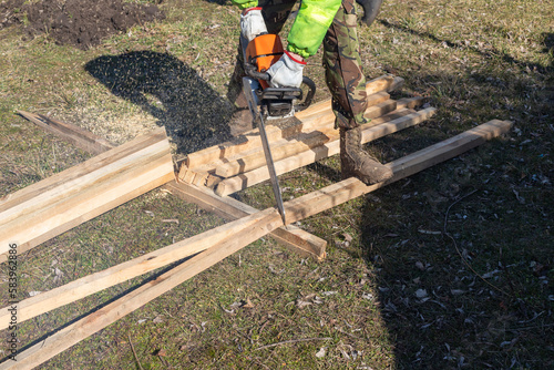 Contractor Worker with Gasoline Chainsaw Cutting Wood Beams.