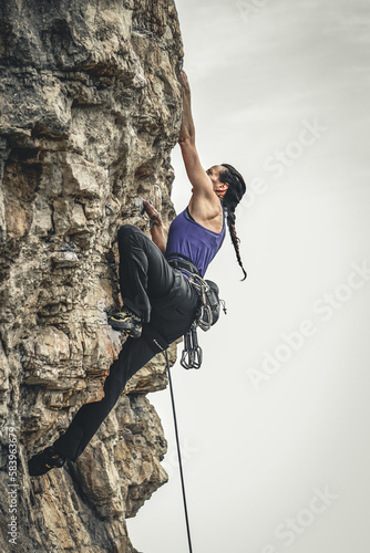 Beautiful black-haired woman with ponytail practicing climbing as a sport. Concept of extreme sports and risk.