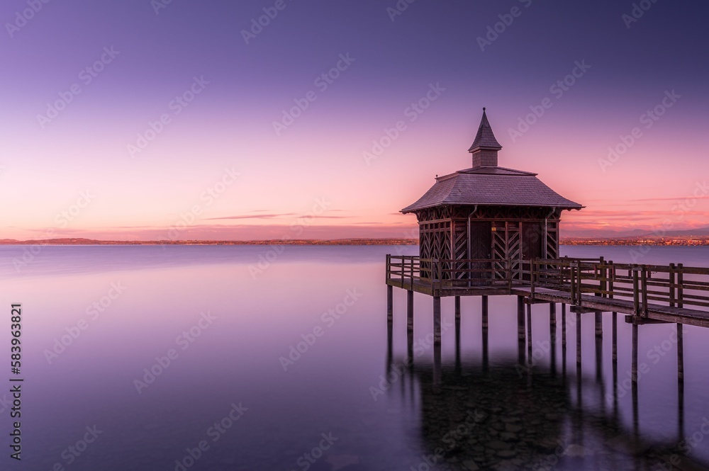 Scenic shot of a gazebo overlooking a calm lake under a gradient sky during dusk