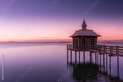 Scenic shot of a gazebo overlooking a calm lake under a gradient sky during dusk