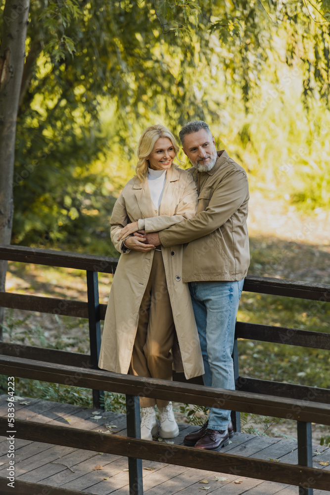 Mature man hugging carefree blonde wife on bridge in spring park. Mature man hugging carefree blonde wife on bridge in spring park.