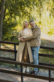 Mature man hugging carefree blonde wife on bridge in spring park.