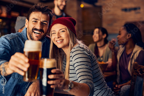 Young couple has fun while toasting with beer in bar and looking at camera.