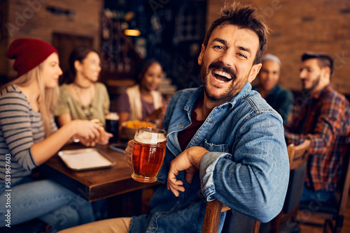 Cheerful man drinks beer and has fun with friends in pub.
