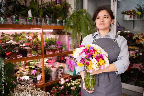 Beautiful woman of Asian appearance holding a bouquet of alstroemeria in a flower shop. Identity, ethnicity, small business, florist, professional, mothers day, spring mood, fragrance, perfume