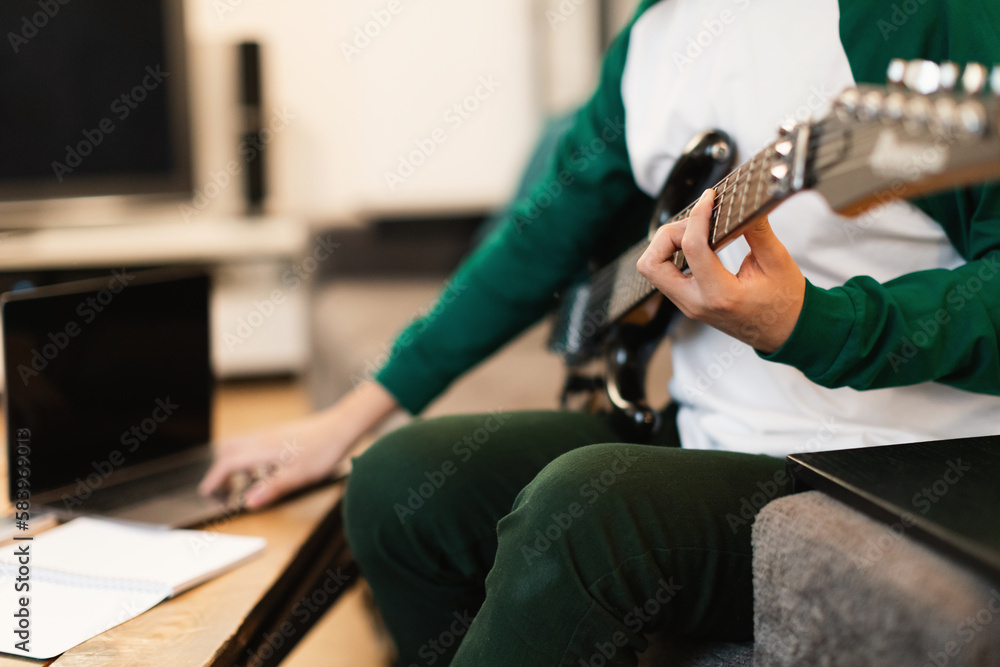 Guy Playing Electric Guitar And Browsing On Laptop Indoor, Cropped