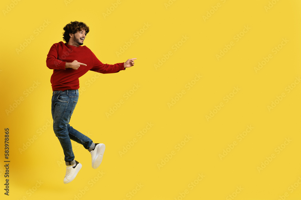 Cheerful young eastern guy jumping up, pointing at copy space Cheerful young eastern guy jumping up, pointing at copy space