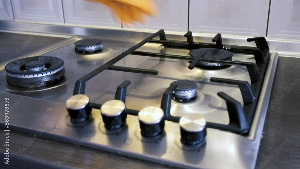 A man wearing protective gloves puts cast-iron grates on a stainless steel gas surface and wipes them clean of dirt with a kitchen sponge. Up close A man wearing protective gloves puts cast-iron grates on a stainless steel gas surface and wipes them clean of dirt with a kitchen sponge. Up close