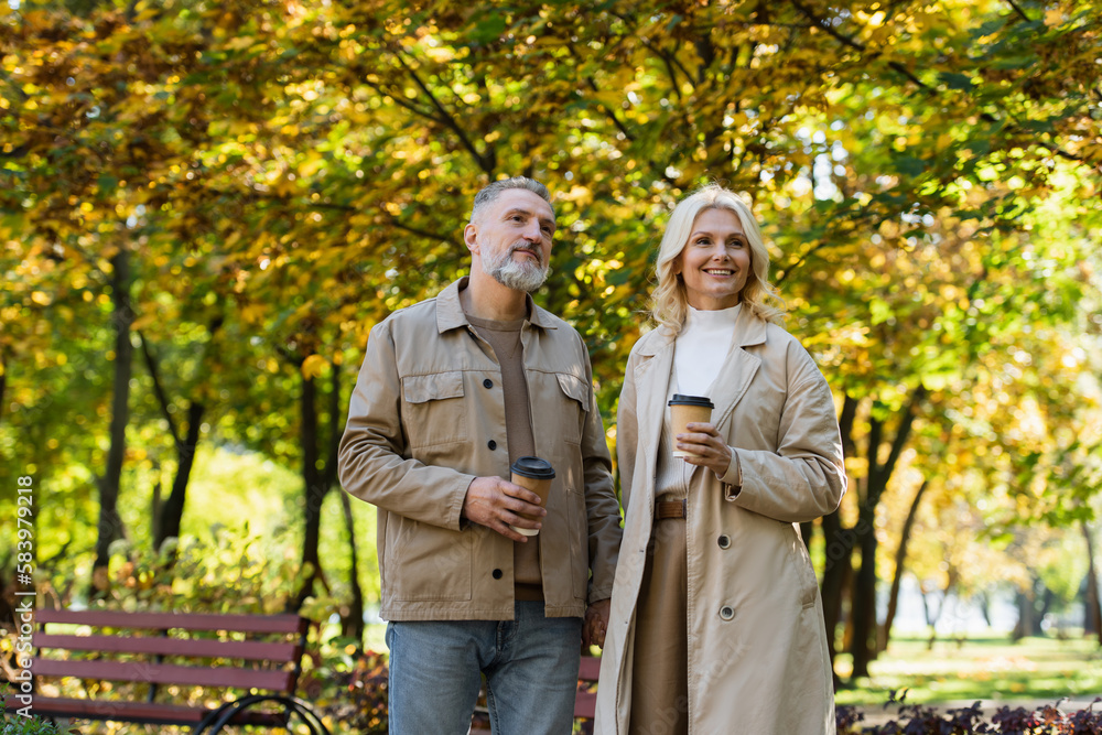 Positive mature couple holding paper cups while walking in park. Positive mature couple holding paper cups while walking in park.
