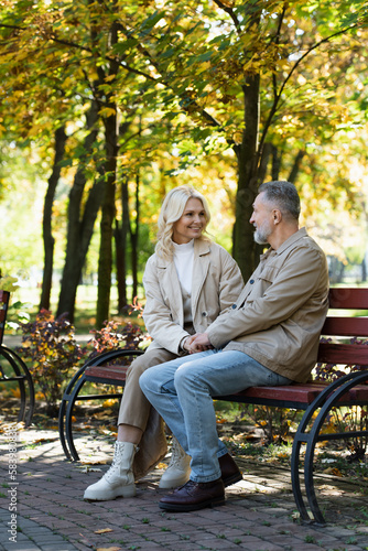 Cheerful mature couple talking on bench in autumn park.