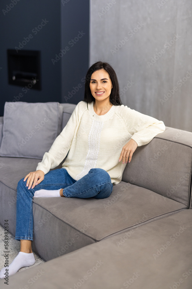 Smiling pretty young woman wearing casual clothes relaxing on a couch at home