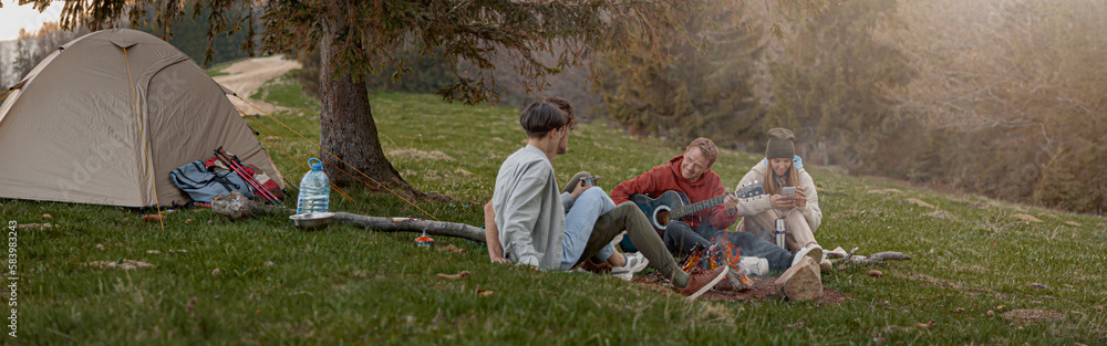 Caucasian team of friends hikers resting with guitar playing at tent in mountains. . Caucasian team of friends hikers resting with guitar playing at tent in mountains. .