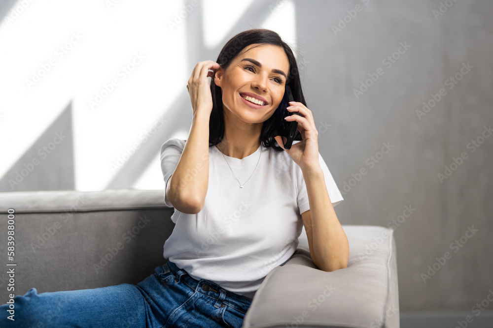 Happy young woman caller talking on the phone at home, cheerful teen girl enjoys pleasant mobile conversation in living room Happy young woman caller talking on the phone at home, cheerful teen girl enjoys pleasant mobile conversation in living room