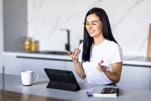 Attractive woman talks with client by tablet makes video call home over blurry kitchen. Successful businesswoman disputes with partner via internet. Lawyer remote consulting.