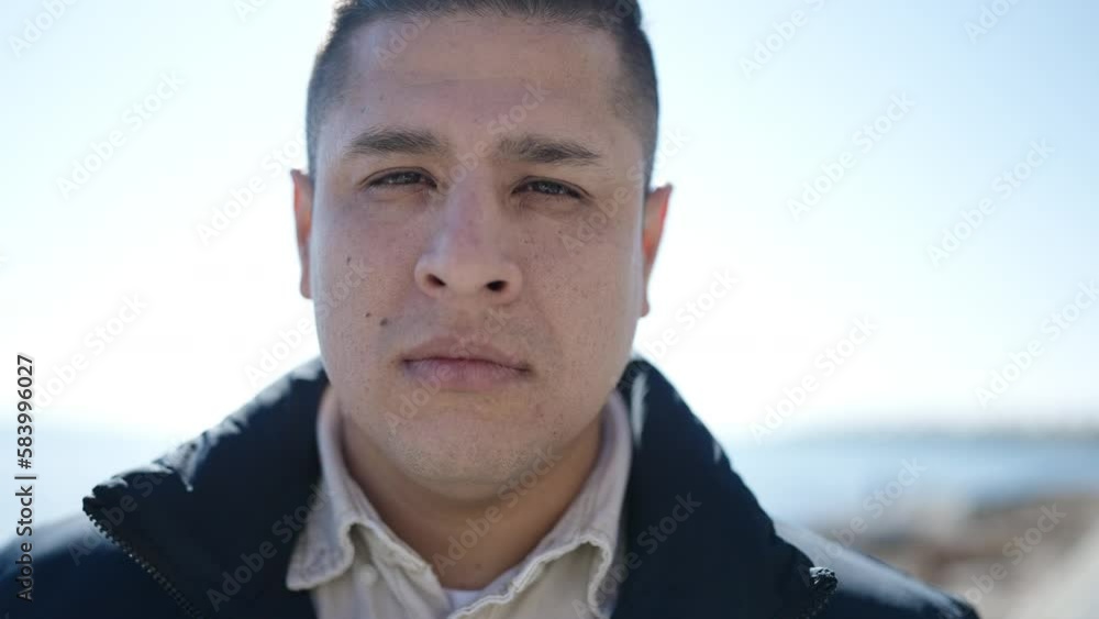 Young hispanic man standing with serious expression at seaside Young hispanic man standing with serious expression at seaside