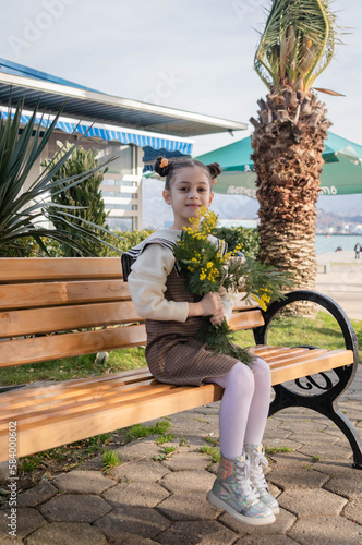Early spring in the park. Child sitting on a bench with a bouquet of mimosa