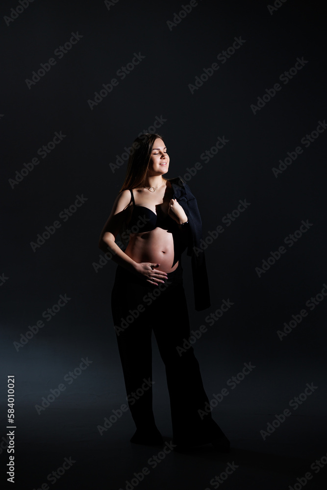 Elegant pregnant woman. Beautiful pregnant girl with long hair in black suit on gray background, concept of happy pregnancy and family.