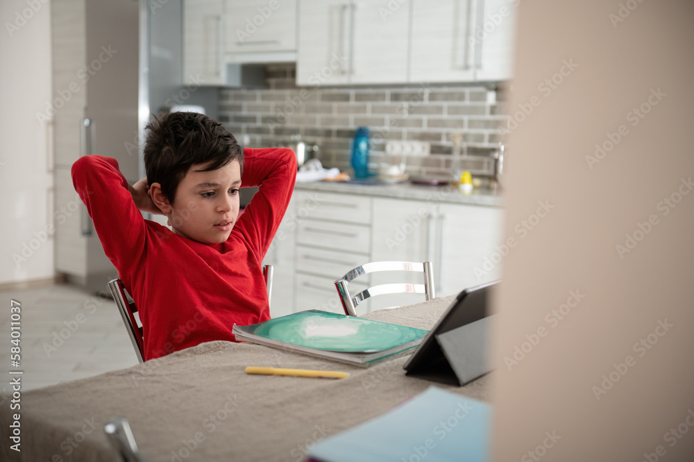 Relaxed Caucasian teenage boy studying online, watching webinar, video lesson on a digital tablet at home. People. Knowledge. E-learning. Education. Back to school on new semester of academic year Relaxed Caucasian teenage boy studying online, watching webinar, video lesson on a digital tablet at home. People. Knowledge. E-learning. Education. Back to school on new semester of academic year