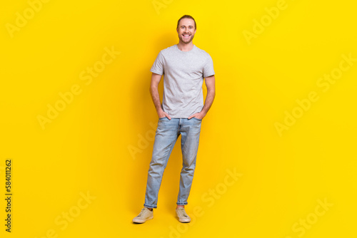 Full length photo of cheerful satisfied guy dressed light t-shirt standing hold hands in pockets isolated on yellow color background