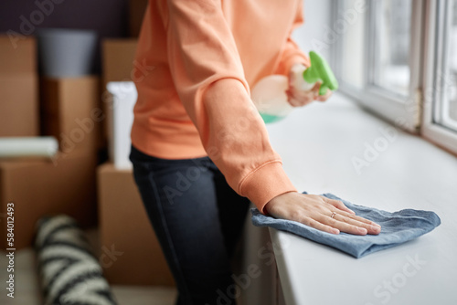 Close-up of young woman wiping dust from windowsill with rag during housework at home photo
