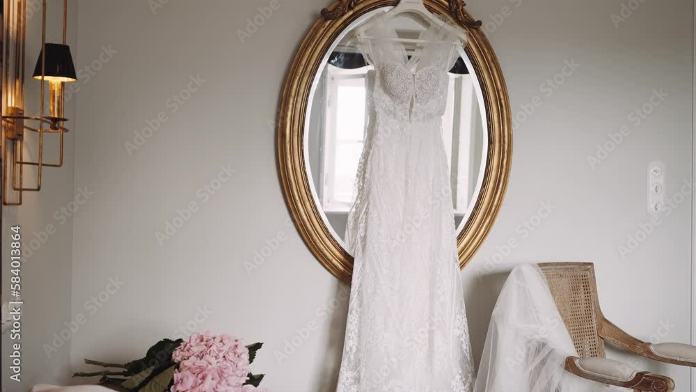 Long wedding dress hangs on mirror golden frame in room Long wedding dress hangs on mirror golden frame in room