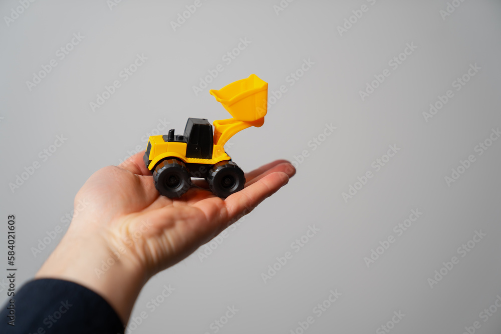 Fototapeta premium Hand holding yellow mini construction bulldozer 