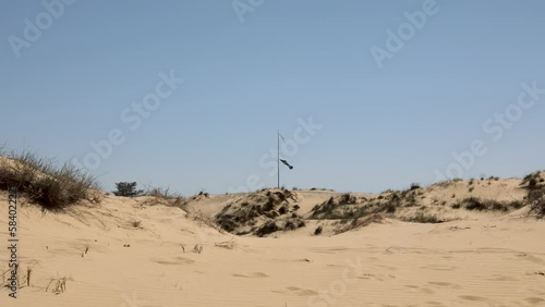 The dunes of Europe's largest desert, the Oleshki sands, tattered flags on an old flagpole on a hot summer day, poor green vegetation photo