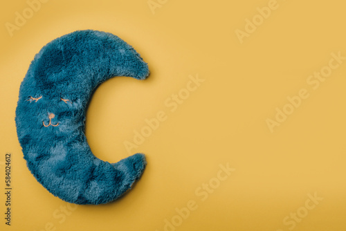 Fototapeta Naklejka Na Ścianę i Meble -  Blue soft moon shaped pillow on yellow background. Top view, copy space