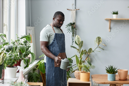 Portrait of adult black man caring for plants indoors and wearing apron