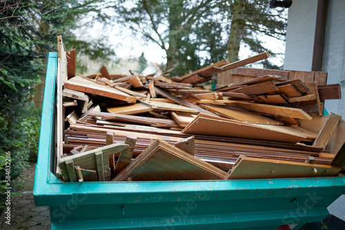 green recycling container filled with wood, next to a house