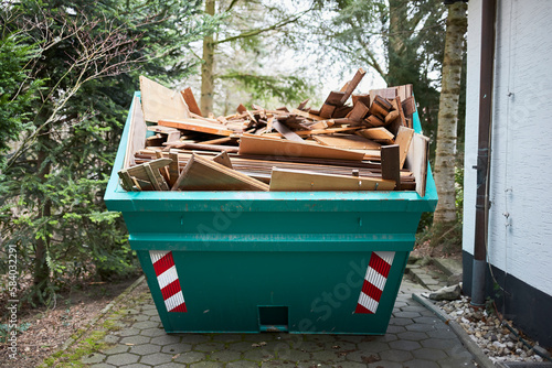 green container filled with wood, next to a house