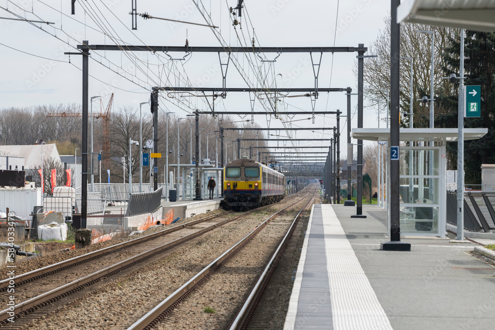 Fototapeta premium View of a belgian train standing on the platform in Diepenbeek, and public work performed at the side of the rail track.