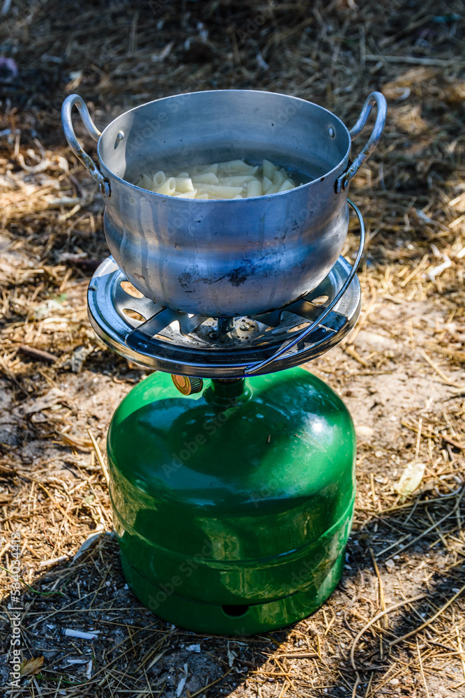 Pasta cooking in aluminium pan on a portable gas stove. Bushcraft or camping concept Pasta cooking in aluminium pan on a portable gas stove. Bushcraft or camping concept