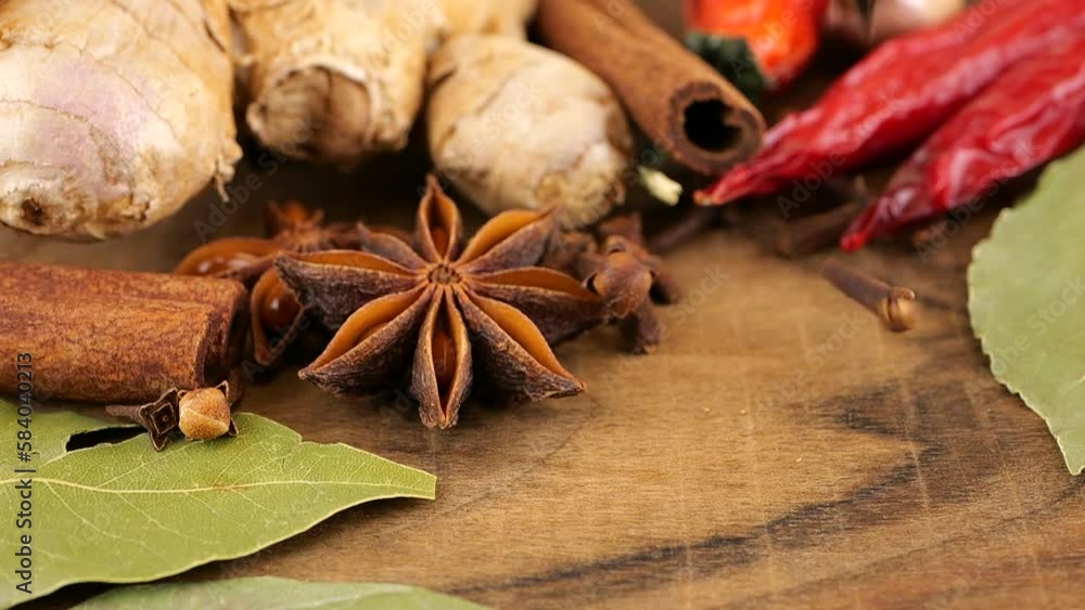 Falling dried clove buds on a wooden board against the background of ginger root, red chili pepper, star anise, bay leaf and garlic. Falling dried clove buds on a wooden board against the background of ginger root, red chili pepper, star anise, bay leaf and garlic.