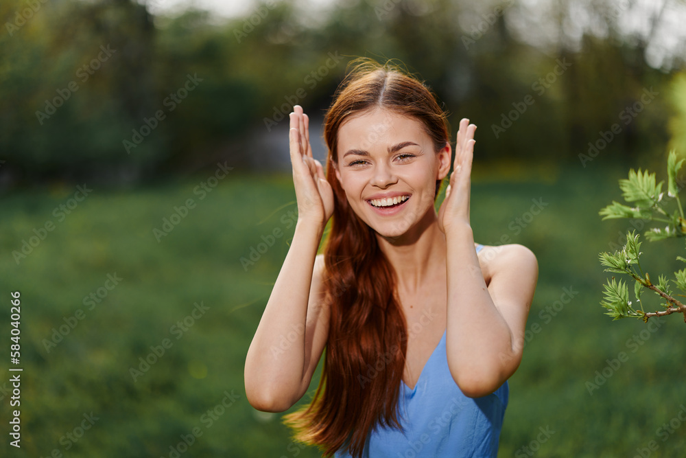 Woman in the summer outdoors smile with teeth stroking long natural hair and happy, the concept of a healthy body and healthy hair in the spring and summer in the sun