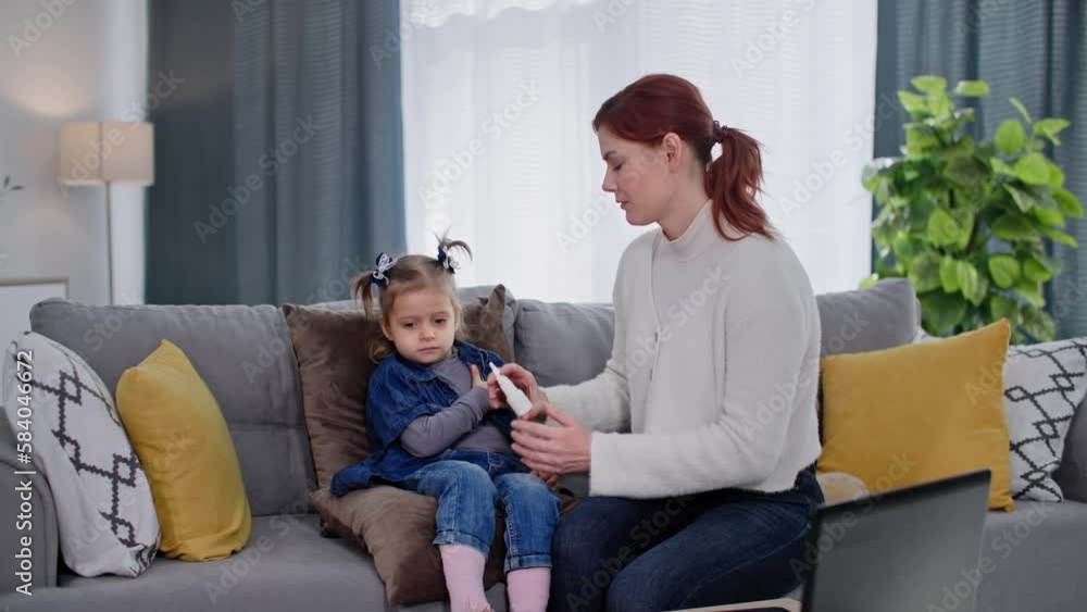 flu and sickness, loving female parent coaxing little girl begin to drip cold medicine while sitting on couch at home flu and sickness, loving female parent coaxing little girl begin to drip cold medicine while sitting on couch at home