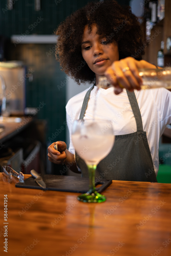 Portrait of young African female bartender preparing a drink at the bar of a restaurant.