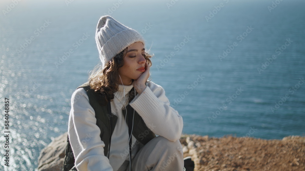 Serene girl enjoying music on ocean cliff. Dreamy woman relax with closed eyes