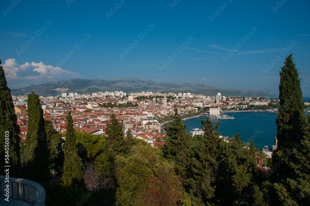 A balcony overlooking a forest, the city of split and a bay with ships in the harbor