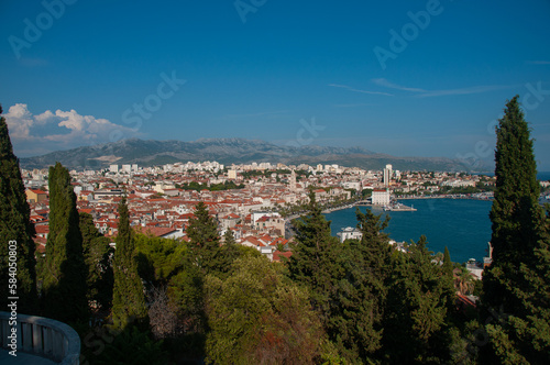 A balcony overlooking a forest, the city of split and a bay with ships in the harbor