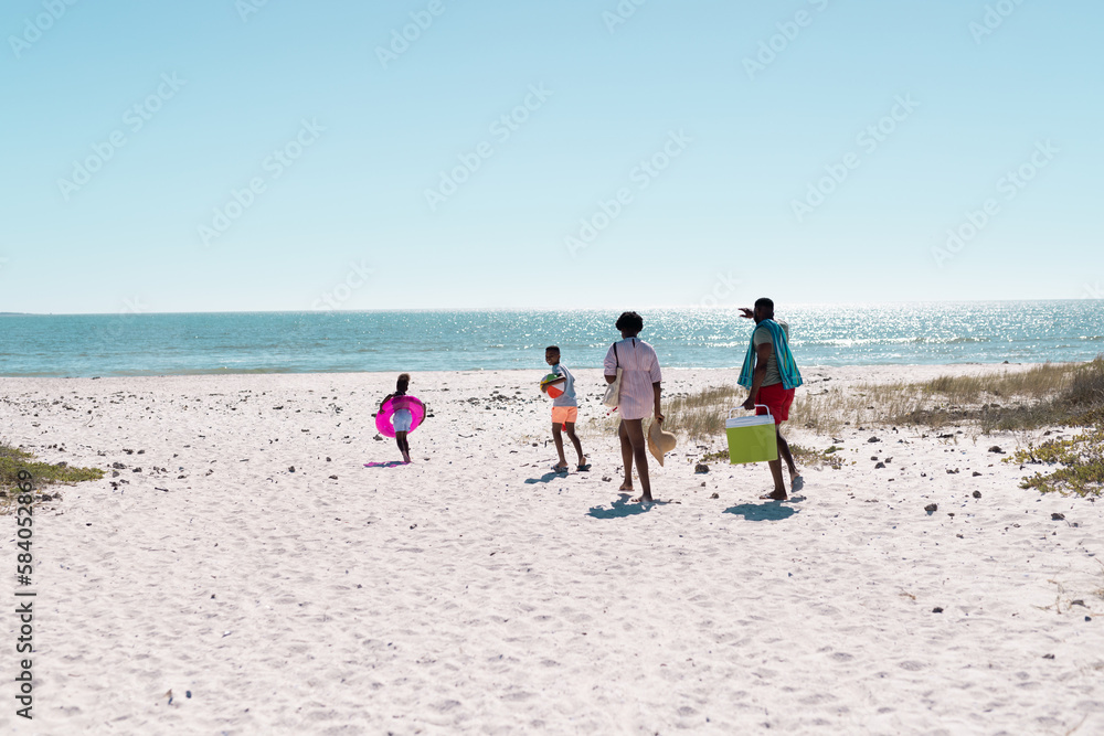 African american parents walking and playful children running on beach against clear sky in summer