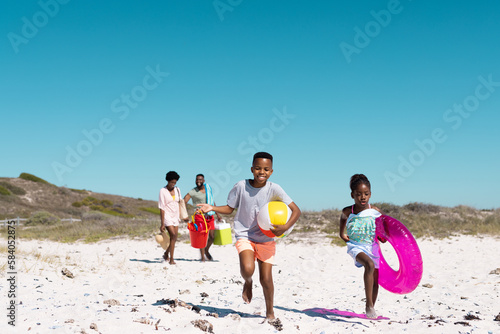 Murais de parede African american playful children running and parents walking on sandy beach und