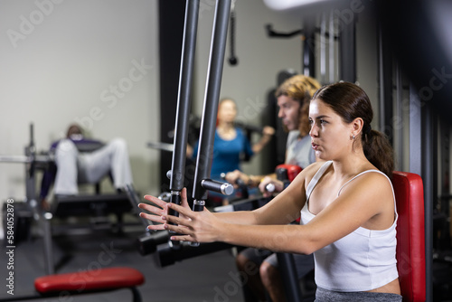 Sporty woman works on special simulator for the development of pectoral muscles