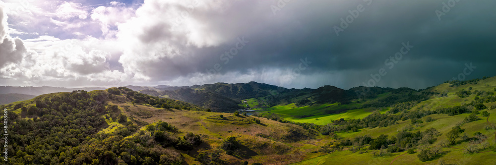 Panoramic view of bright sun and dark storm clouds over green California landscape